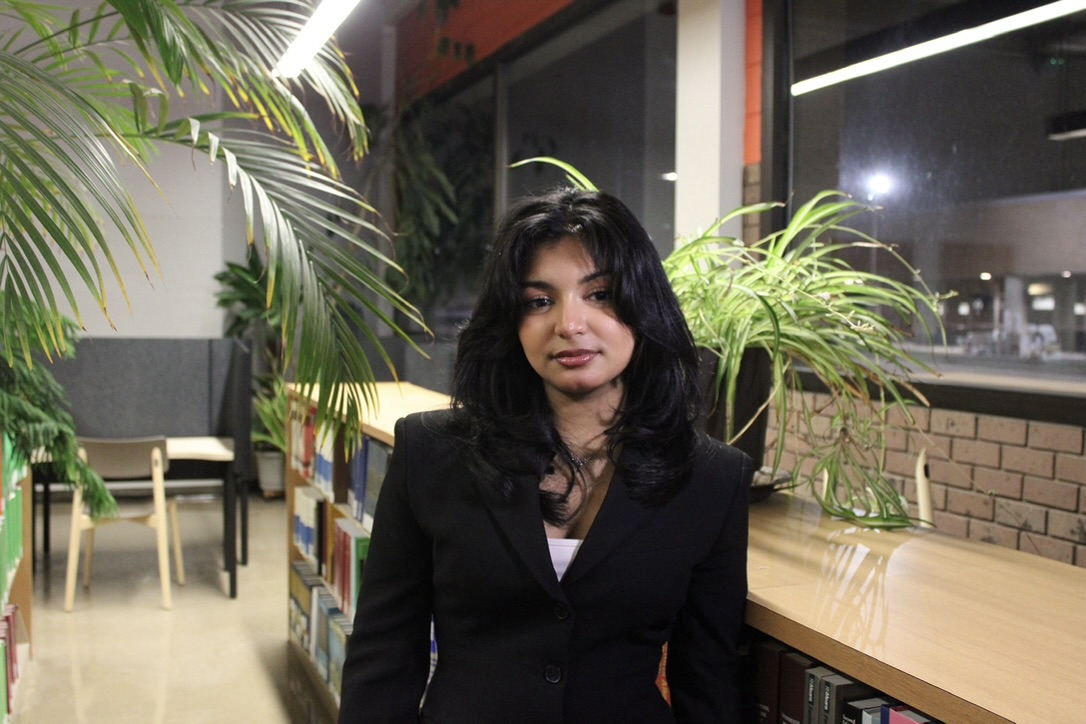 Leya Skaria wearing a black blazer, seated beside plants and a window